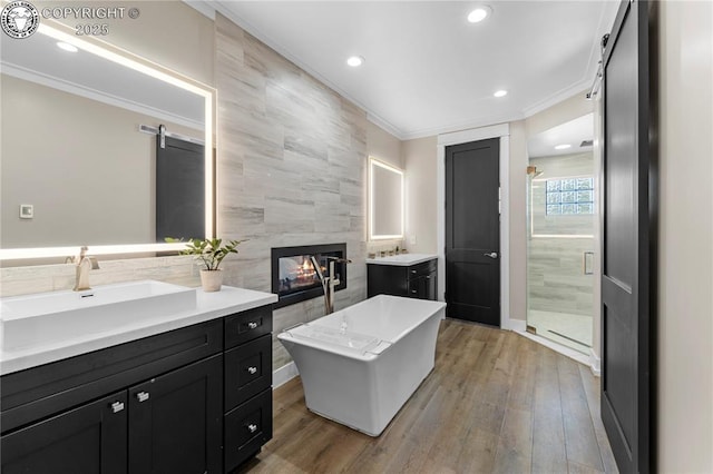 bathroom featuring a soaking tub, ornamental molding, wood finished floors, vanity, and a multi sided fireplace