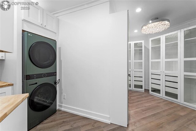 laundry area with laundry area, recessed lighting, stacked washer / drying machine, and wood finished floors