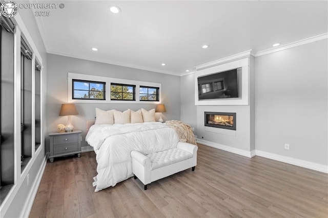 bedroom with wood finished floors, recessed lighting, a glass covered fireplace, and crown molding