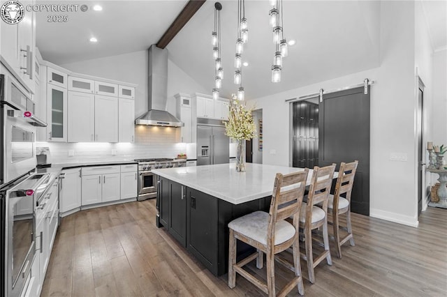 kitchen with a center island, a barn door, white cabinets, high quality appliances, and wall chimney exhaust hood