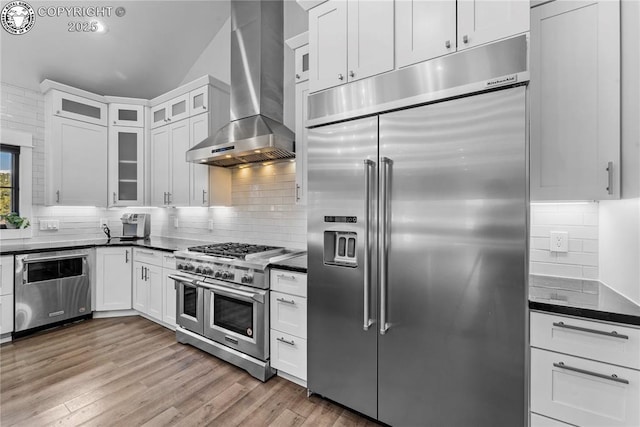 kitchen with high end appliances, white cabinetry, glass insert cabinets, and wall chimney range hood