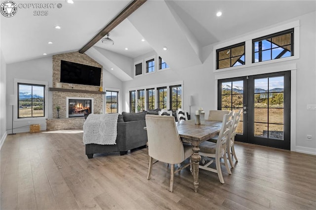 dining space with a large fireplace, french doors, light wood-type flooring, and beam ceiling