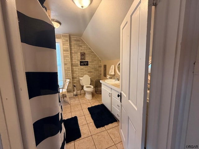 bathroom with lofted ceiling, vanity, brick wall, tile patterned floors, and toilet