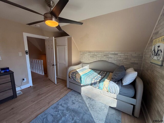 bedroom featuring ceiling fan, brick wall, light hardwood / wood-style floors, and lofted ceiling