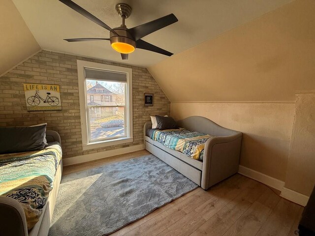 bedroom with vaulted ceiling, brick wall, ceiling fan, and light hardwood / wood-style floors