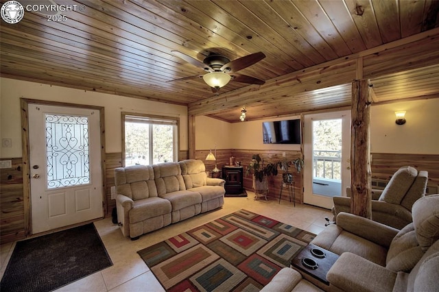 tiled living room with ceiling fan, a wood stove, wooden ceiling, and wooden walls