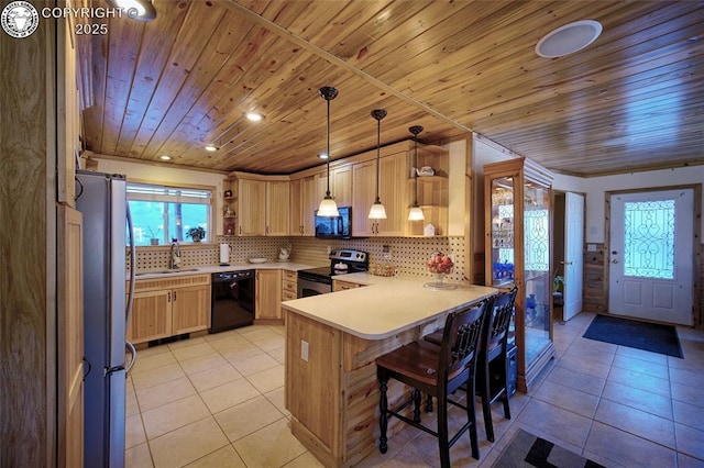 kitchen featuring a breakfast bar, black appliances, light brown cabinetry, decorative light fixtures, and kitchen peninsula