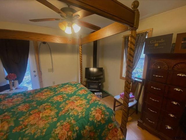 bedroom featuring hardwood / wood-style flooring, ceiling fan, and a wood stove