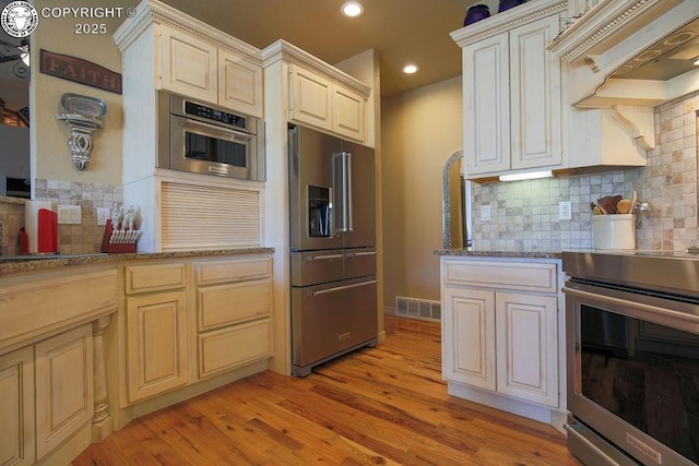 kitchen with stainless steel appliances, visible vents, cream cabinetry, light wood-type flooring, and custom range hood