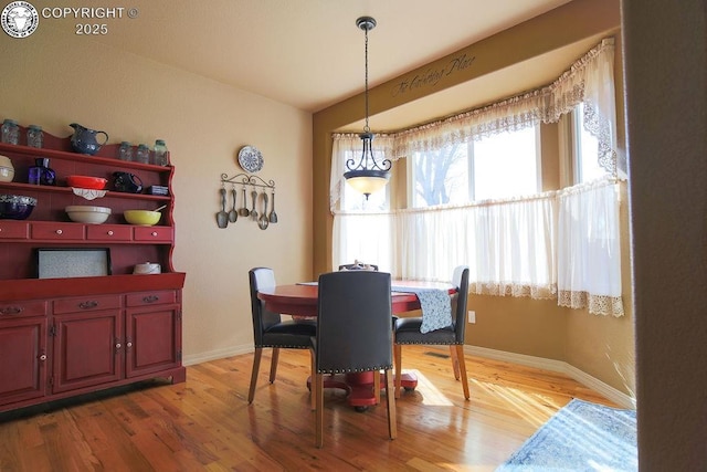 dining area with light wood-style floors, baseboards, and vaulted ceiling