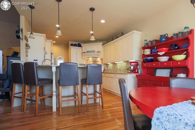 kitchen with pendant lighting, cream cabinetry, light wood-style flooring, and open shelves