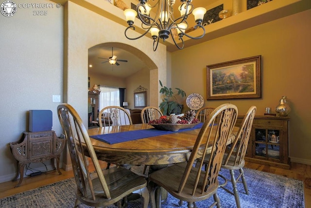 dining room with ceiling fan with notable chandelier, arched walkways, baseboards, and wood finished floors