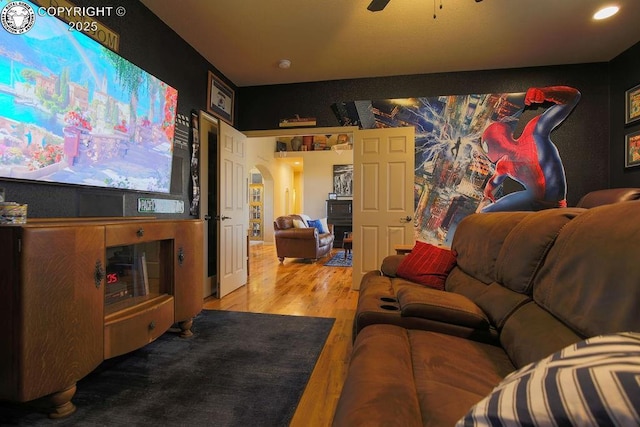 cinema with arched walkways, ceiling fan, and wood finished floors