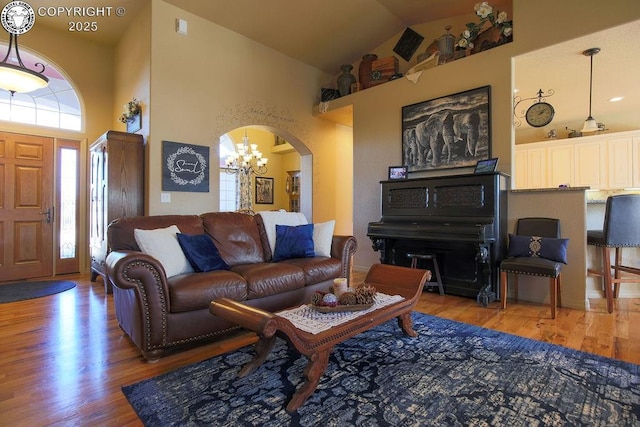 living room with high vaulted ceiling, arched walkways, a chandelier, and light wood-style flooring