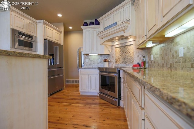 kitchen with visible vents, decorative backsplash, appliances with stainless steel finishes, light wood-style floors, and premium range hood