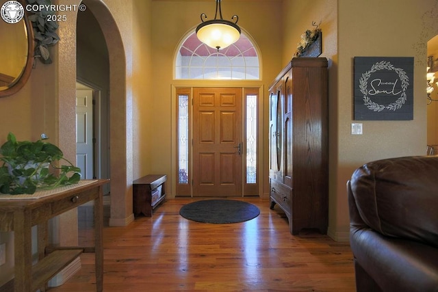 entrance foyer with baseboards, arched walkways, a wealth of natural light, and wood finished floors