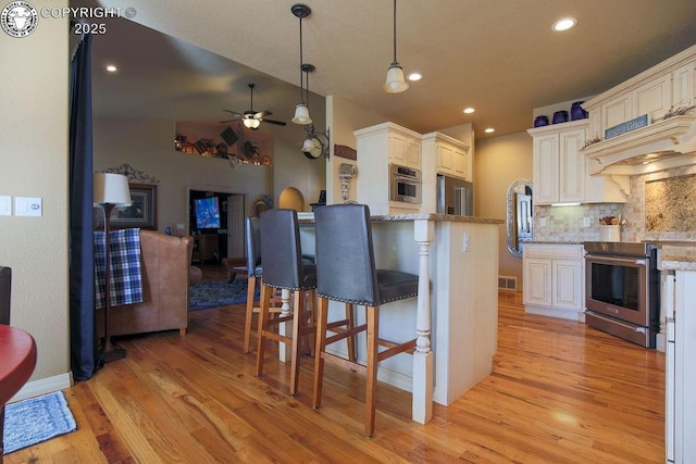 kitchen featuring open floor plan, stainless steel appliances, pendant lighting, and light stone countertops