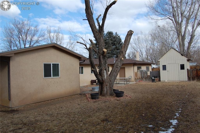 back of property with an outbuilding, stucco siding, fence, and a shed