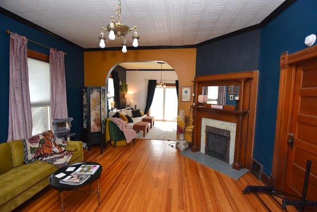 living room with crown molding, wood-type flooring, a chandelier, and a tiled fireplace