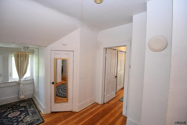 corridor with wood-type flooring and vaulted ceiling