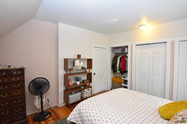 bedroom featuring hardwood / wood-style flooring, vaulted ceiling, and two closets