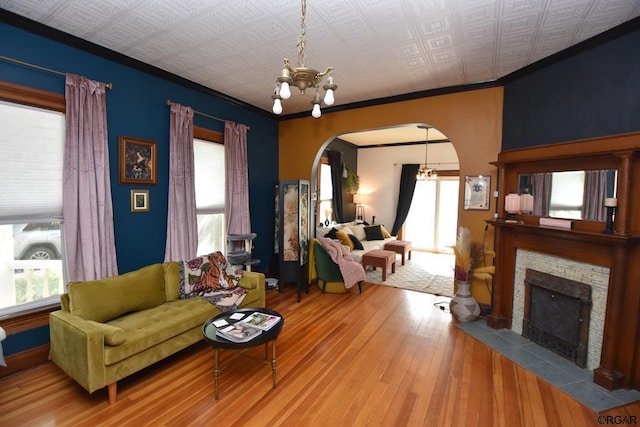 living room featuring an inviting chandelier, ornamental molding, wood-type flooring, and a stone fireplace