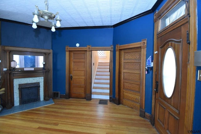 foyer entrance featuring crown molding, hardwood / wood-style flooring, a fireplace, and a chandelier