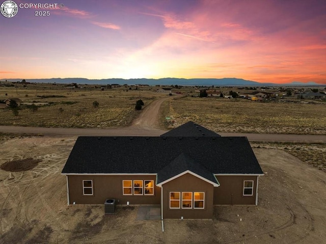 back house at dusk with central AC, a mountain view, and a patio