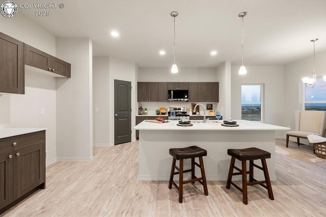 kitchen featuring dark brown cabinetry, stainless steel appliances, an island with sink, and a kitchen bar