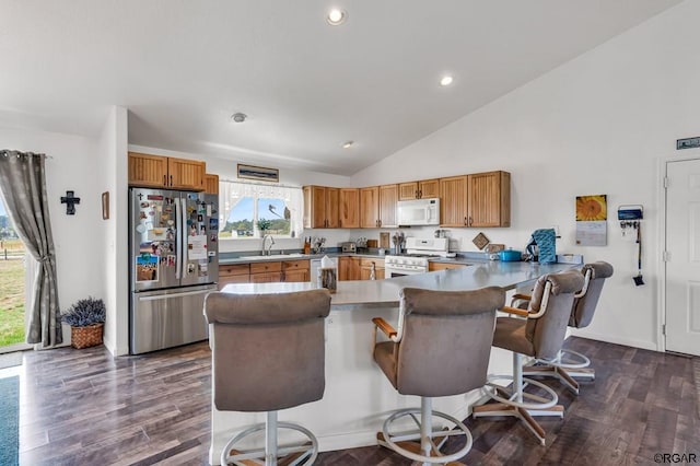 kitchen with a breakfast bar, sink, dark hardwood / wood-style flooring, kitchen peninsula, and white appliances