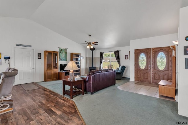 living room with ceiling fan, high vaulted ceiling, light carpet, and a wood stove