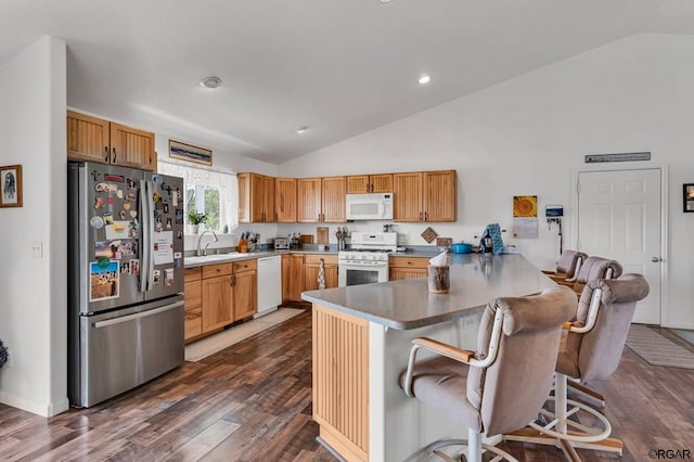 kitchen featuring a breakfast bar, sink, dark hardwood / wood-style flooring, kitchen peninsula, and white appliances