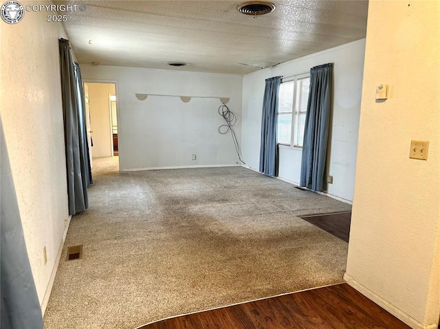 carpeted empty room featuring visible vents, wood finished floors, and a textured wall