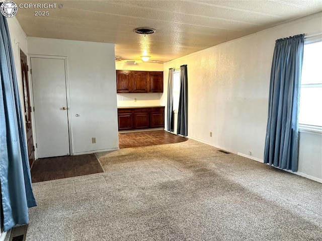 interior space with carpet, visible vents, baseboards, and a textured wall