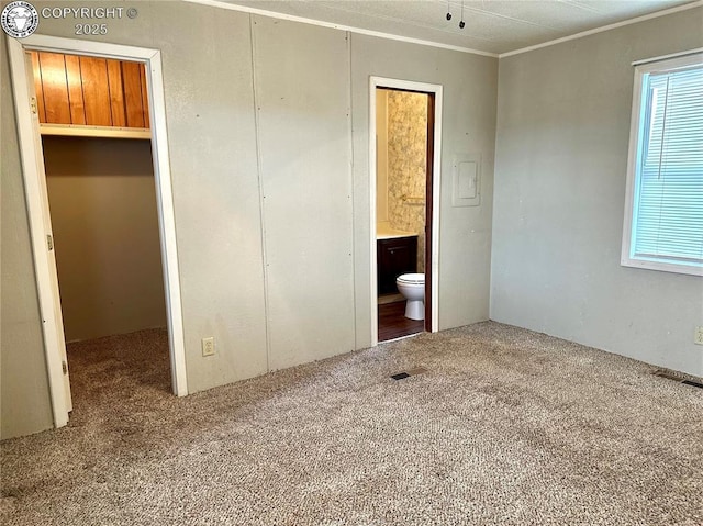 unfurnished bedroom featuring visible vents, ornamental molding, ensuite bathroom, carpet floors, and a closet