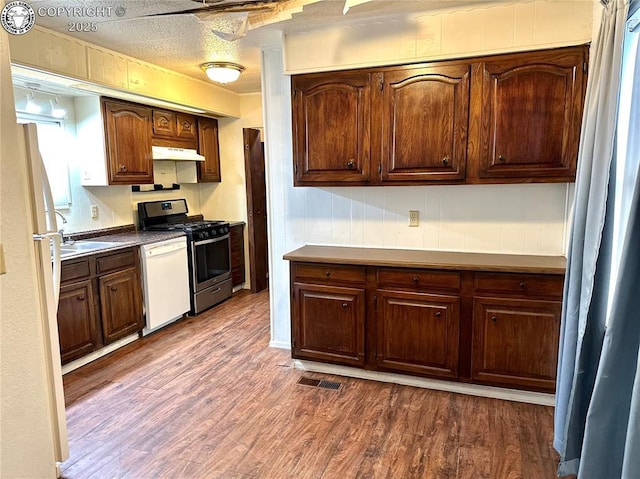 kitchen with white appliances, dark wood-type flooring, a textured ceiling, under cabinet range hood, and a sink