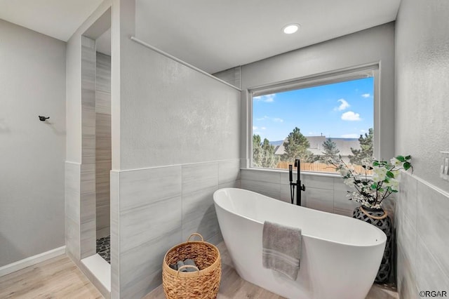 bathroom with hardwood / wood-style flooring, a washtub, and tile walls