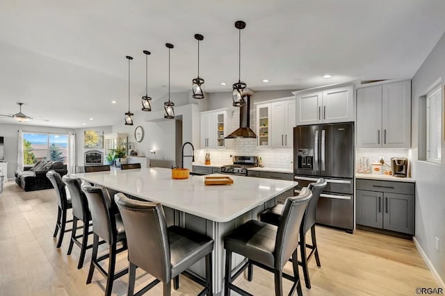 kitchen featuring black fridge with ice dispenser, decorative light fixtures, a kitchen breakfast bar, stainless steel stove, and wall chimney range hood