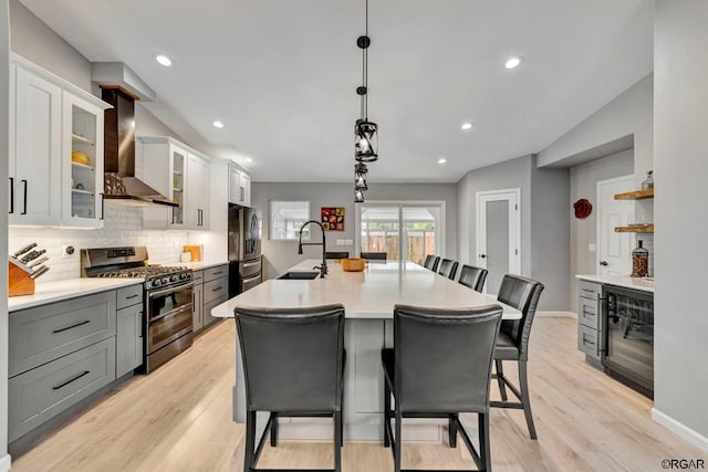 kitchen featuring gray cabinets, appliances with stainless steel finishes, a breakfast bar, pendant lighting, and wall chimney range hood