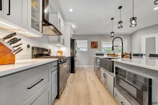 kitchen featuring wall chimney exhaust hood, light wood-type flooring, pendant lighting, stainless steel appliances, and decorative backsplash