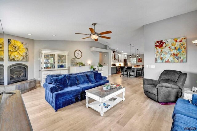 living room featuring a tiled fireplace, lofted ceiling, ceiling fan, and light hardwood / wood-style flooring