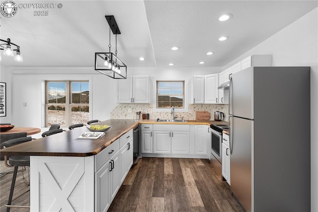 kitchen featuring sink, wooden counters, hanging light fixtures, stainless steel appliances, and white cabinets