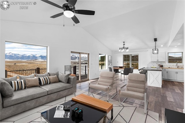 living room with sink, vaulted ceiling, a mountain view, light hardwood / wood-style floors, and ceiling fan with notable chandelier