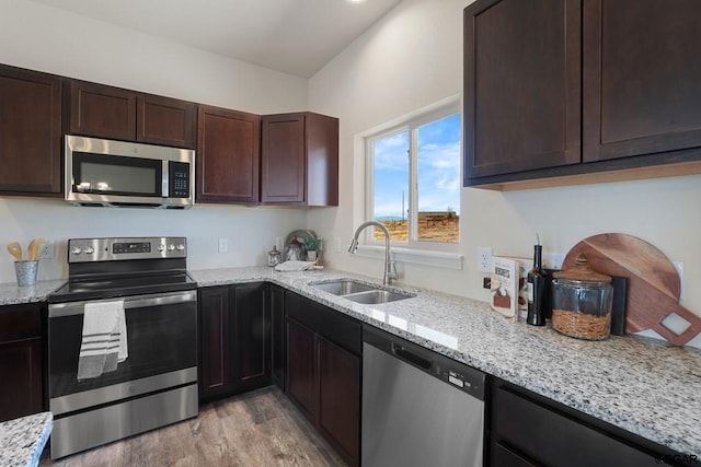 kitchen with dark brown cabinetry, sink, light stone counters, light wood-type flooring, and stainless steel appliances