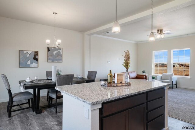 kitchen featuring ceiling fan with notable chandelier, hanging light fixtures, ornamental molding, light stone counters, and dark brown cabinets