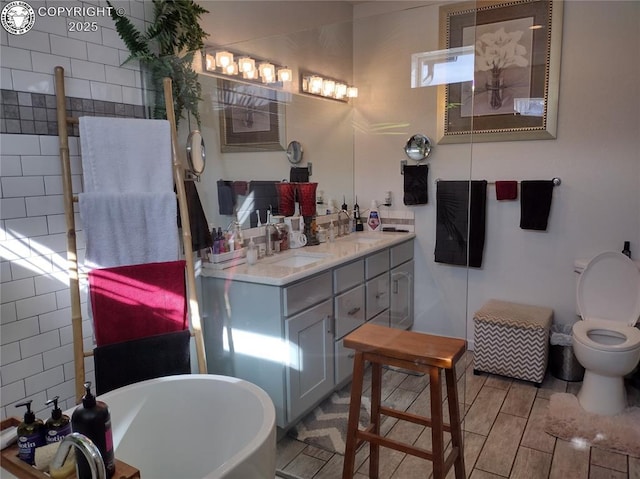 bathroom featuring double vanity, a soaking tub, a sink, and toilet