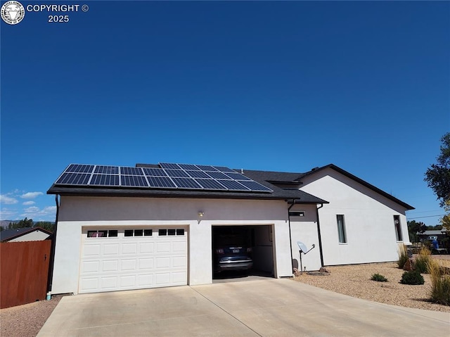 view of property exterior featuring a garage, fence, concrete driveway, roof mounted solar panels, and stucco siding