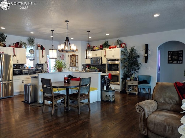 dining space featuring dark wood-style floors, arched walkways, and recessed lighting