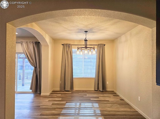 unfurnished dining area featuring an inviting chandelier, wood-type flooring, and a textured ceiling