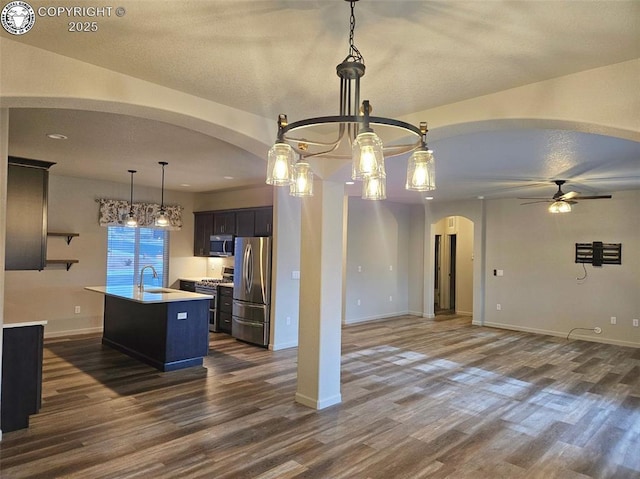 kitchen featuring sink, dark wood-type flooring, hanging light fixtures, stainless steel appliances, and a center island with sink